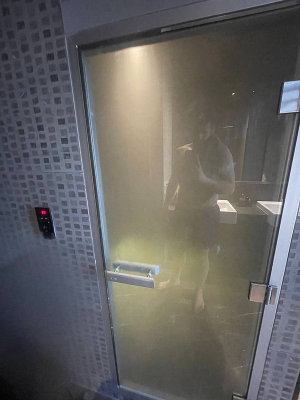 A person stands in front of a fogged glass door leading to a steam room.