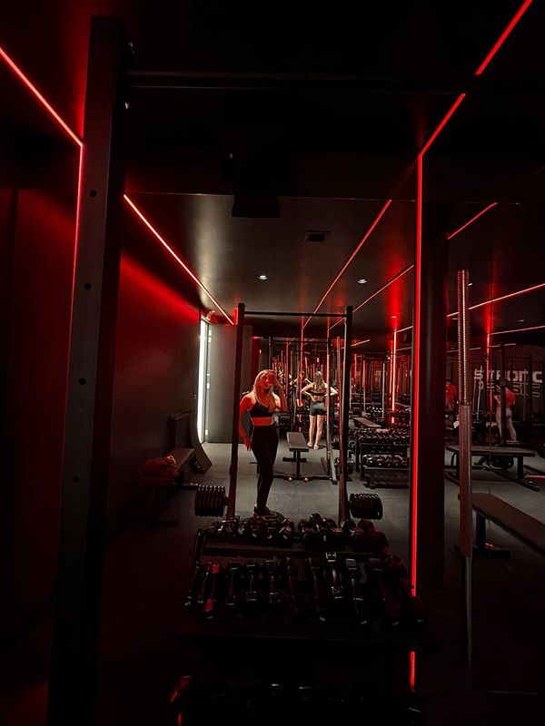 A man in athletic wear is lifting weights in a gym with a pink background and motivational texts on the wall.