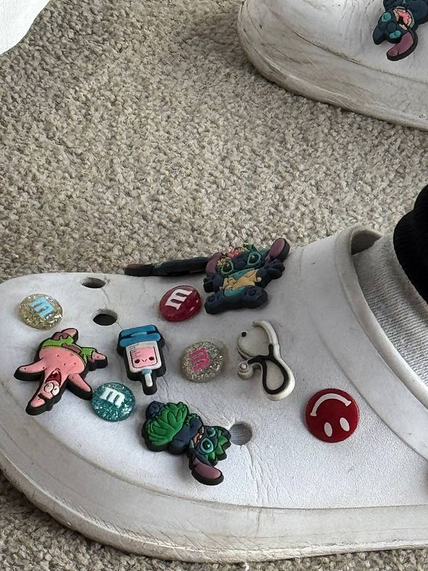 Colorful decorations adorn a pair of white clogs resting on a carpeted surface.