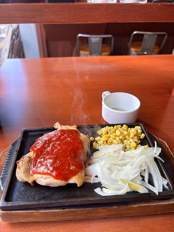 A sizzling chicken steak served on a hot plate with sides of corn and onions.