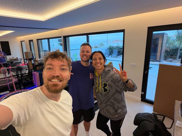 A muscular man in a gym lifting a heavy barbell overhead.