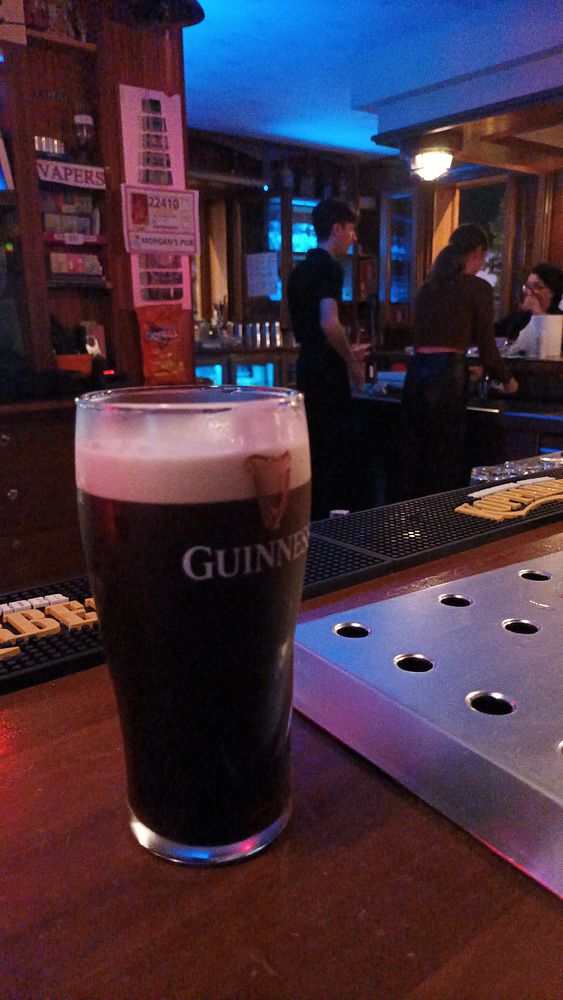 A pint of Guinness is prominently displayed on a bar counter in an Irish pub setting.