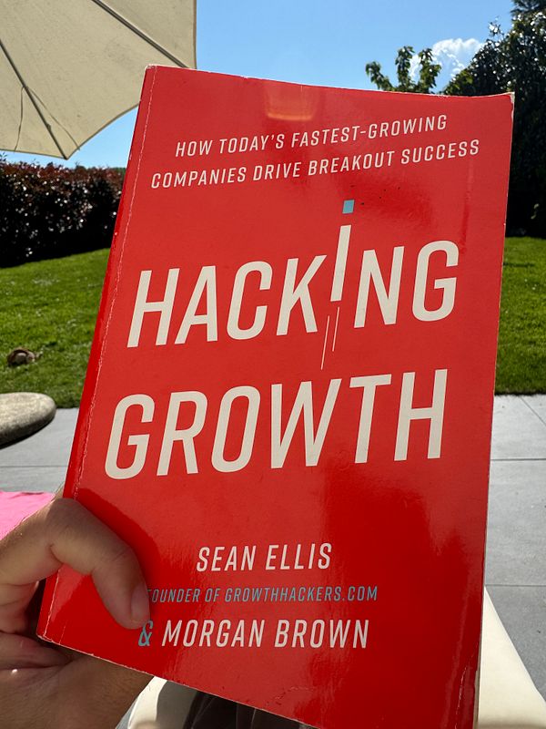 A person is holding the book 'Hacking Growth' in a sunny outdoor setting.