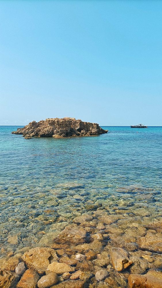 A serene coastal scene featuring clear water and a rocky outcrop.