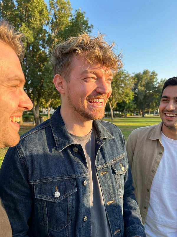 Three young men are smiling and enjoying a sunny day outdoors.