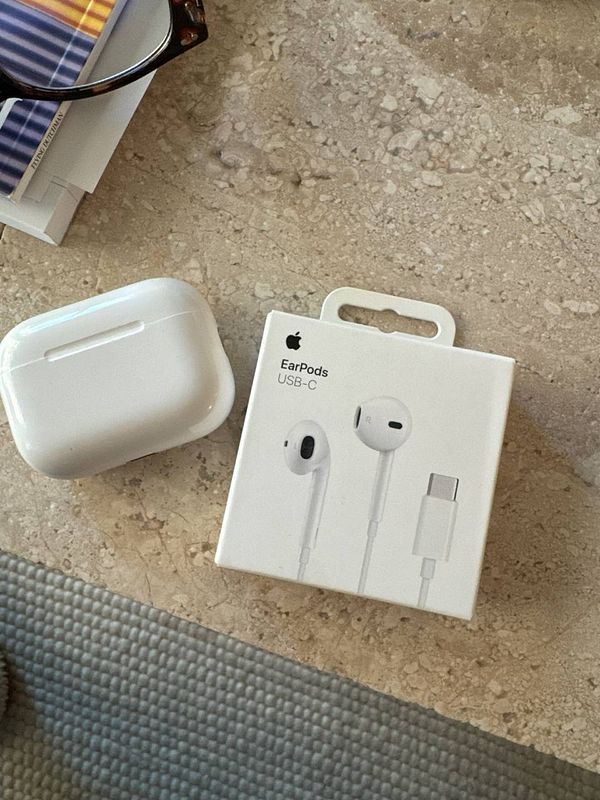 A pair of white Apple EarPods with a USB-C connector on a beige surface.