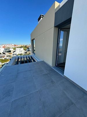 A modern balcony area with a side door leading to a view of nearby houses and a clear blue sky.