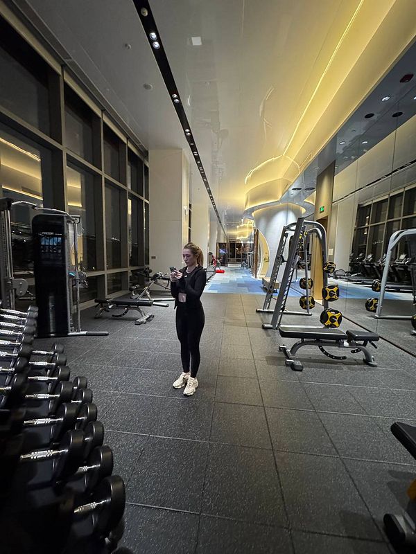 A woman stands in a modern gym, checking her phone amidst various workout equipment.