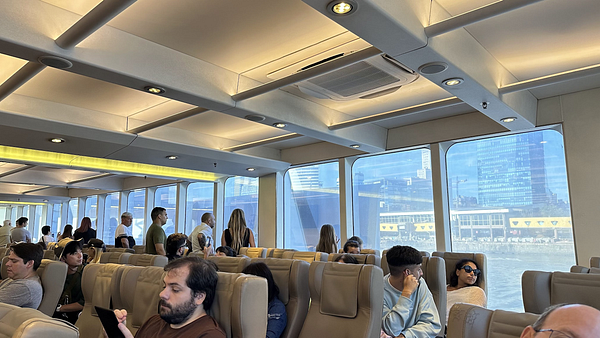 The image captures the interior of a ferry with passengers seated and views of the city outside.