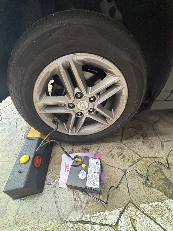 Close-up of a person using a car tire pressure gauge to check a tire's air pressure.