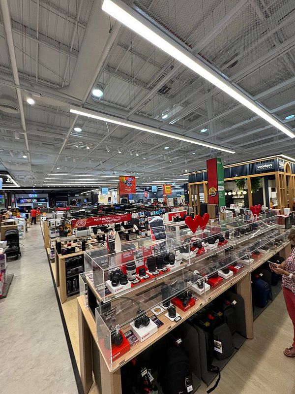 A spacious electronics store interior with various products on display and visible customer activity.