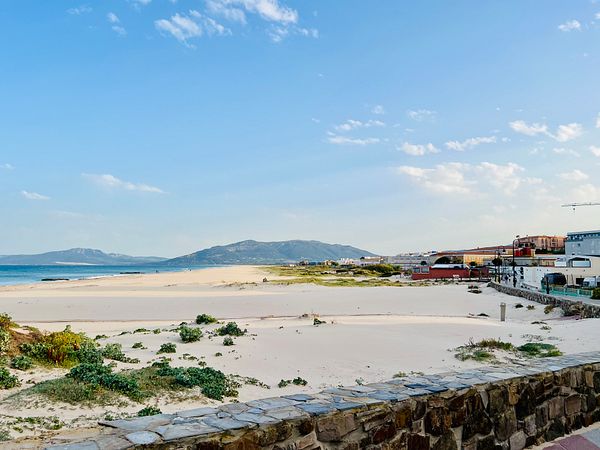 A scenic beach view with mountains in the background and a clear blue sky.