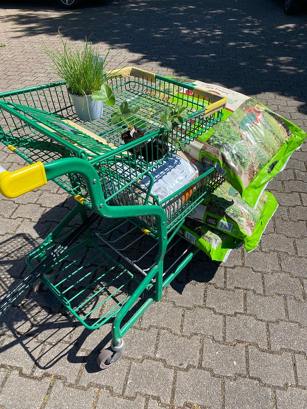 Photograph of various permaculture-related items including fabric rolls, cardboard boxes, and orange women’s high-heeled boots staged on a pavement.