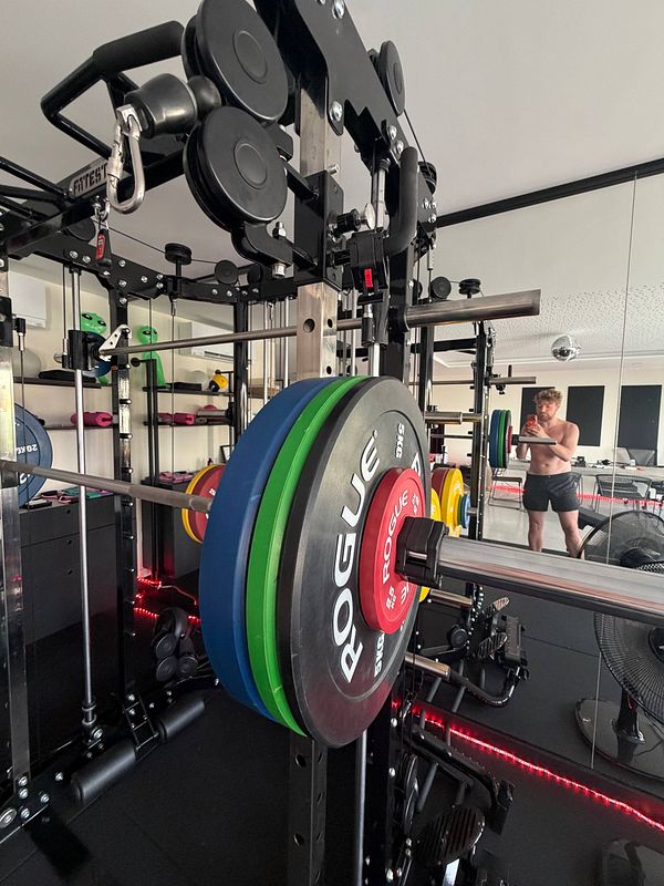 A woman lifting a barbell in a gym setting, focusing on strength training.