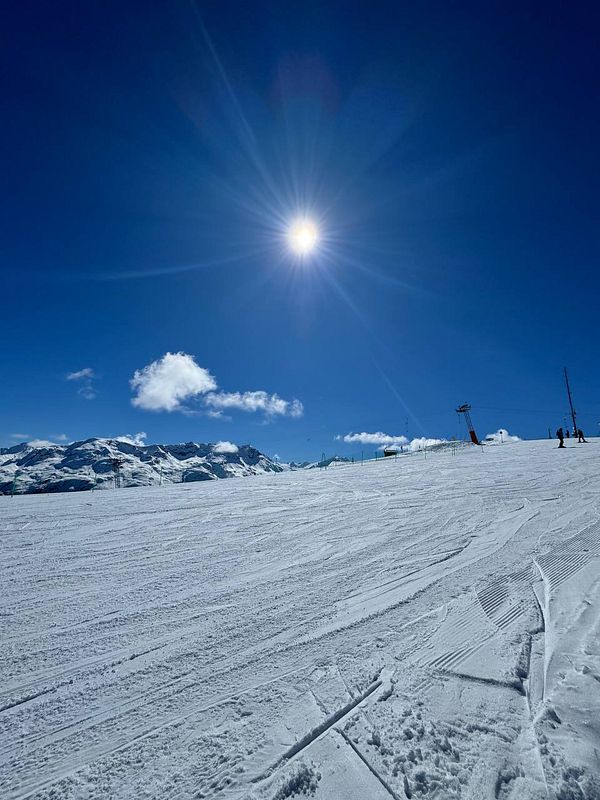 A bright, sunny day on a ski slope with clear blue skies and snow-covered mountains.