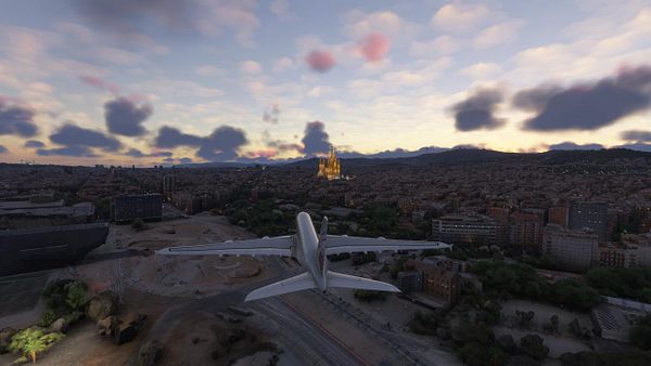 An aircraft is flying over Barcelona at sunset, with the Sagrada Familia visible in the distance.