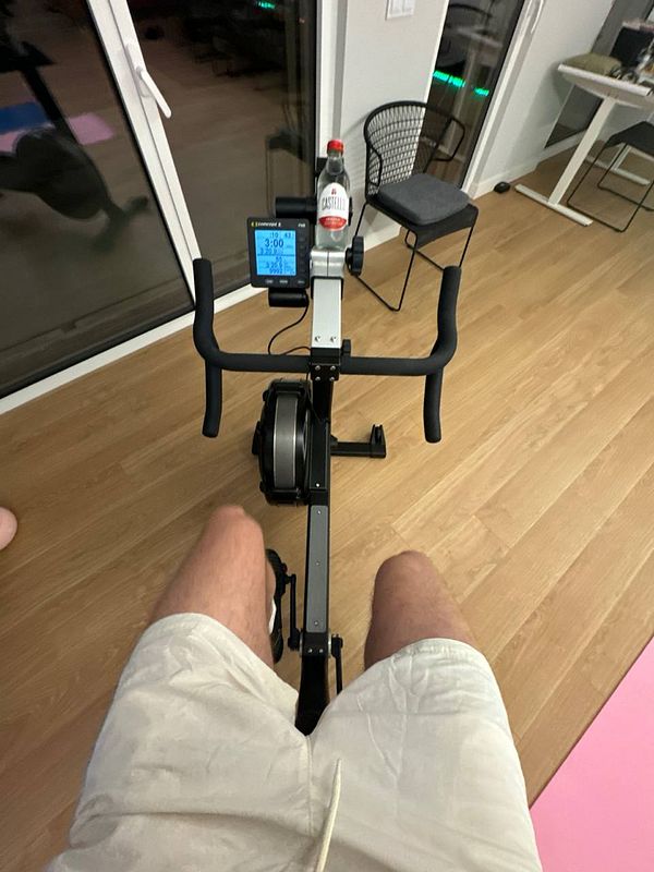 A person is seated on a rowing machine in a home gym setting.