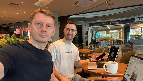 Photo of two young women smiling and posing closely together in an outdoor setting with a city skyline in the background.