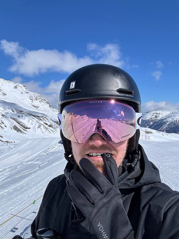 A skier poses on a snowy mountain slope under a clear blue sky.