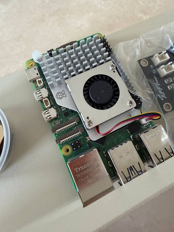 A Raspberry Pi board with a cooling fan and heat sink is displayed on a surface.