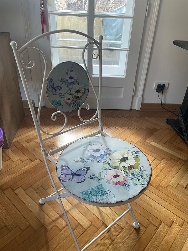 A decorative chair with floral and butterfly designs is positioned in a well-lit room.
