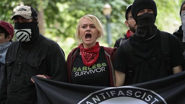 A group of protesters at an Antifa rally, with a focus on a woman in the foreground expressing strong emotions.