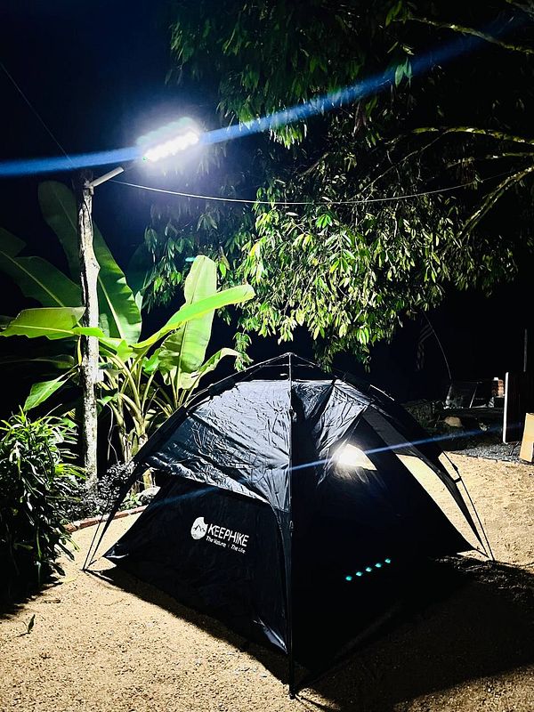 A camping scene at night featuring a black tent illuminated by a bright light.