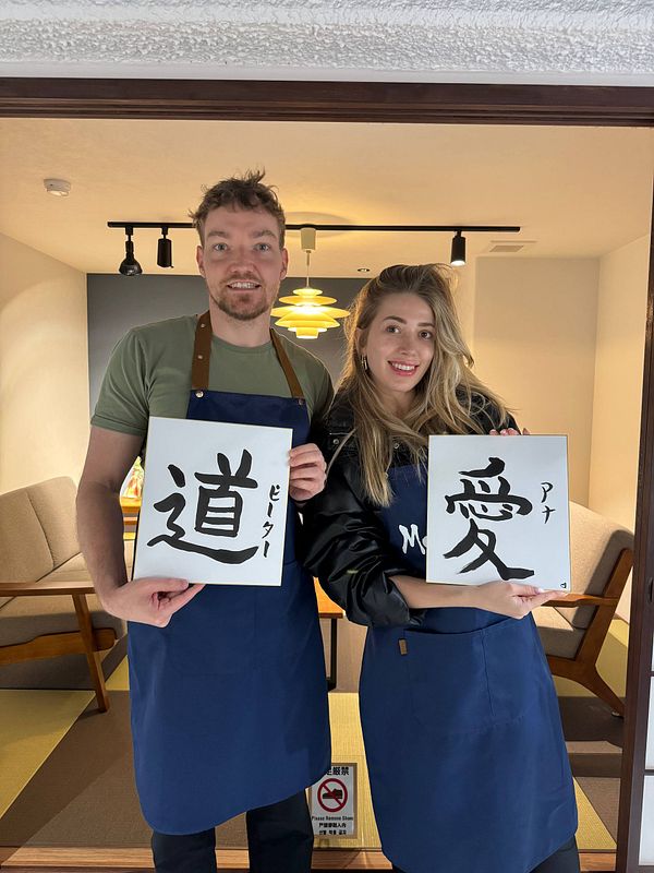 Two individuals are posing with calligraphy artworks in a Japanese setting.