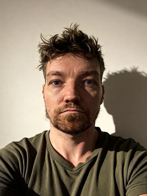 A close-up portrait of a man with tousled hair and a serious expression, illuminated by natural light.