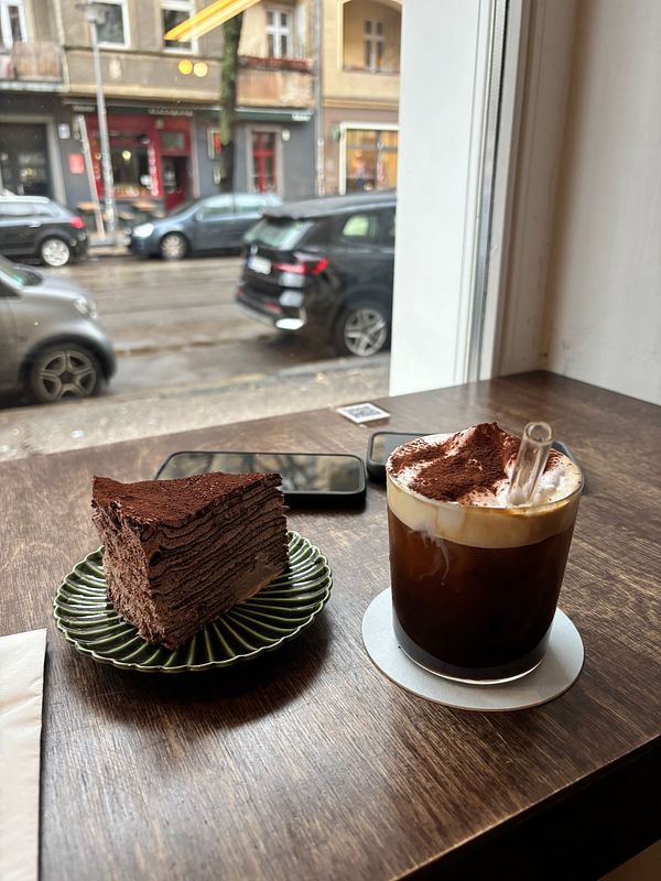 A wooden table setting at a Vietnamese café featuring a white bowl of fried rice with egg, a iced coffee, and a smartphone.