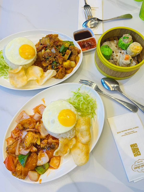 The image features two plates of food, each with a fried egg, rice, and various accompaniments, alongside a bamboo steamer filled with dim sum.
