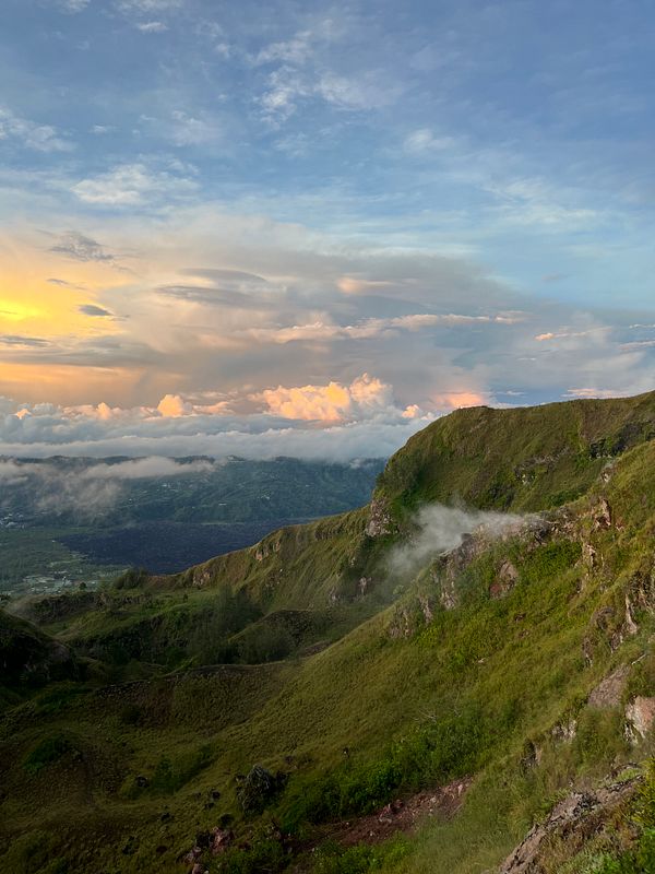 A breathtaking view from Mount Batur showcasing a vibrant sunrise over lush green hills and clouds.