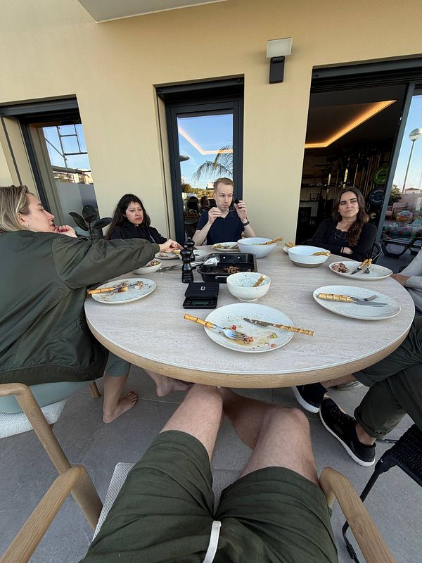 A group of five people sitting around a round table with empty plates and bowls after a meal on a covered patio.