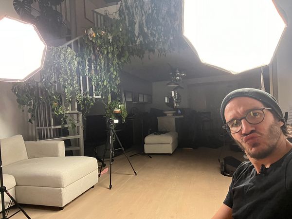 Man sitting in a well-lit room set up for recording a podcast with professional lighting, camera on tripod, and a cozy chair.