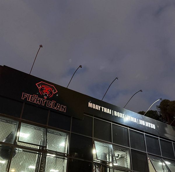 Close-up image of a fist wrapped with traditional Muay Thai hand wraps in red with blue stripes, performing a punch.