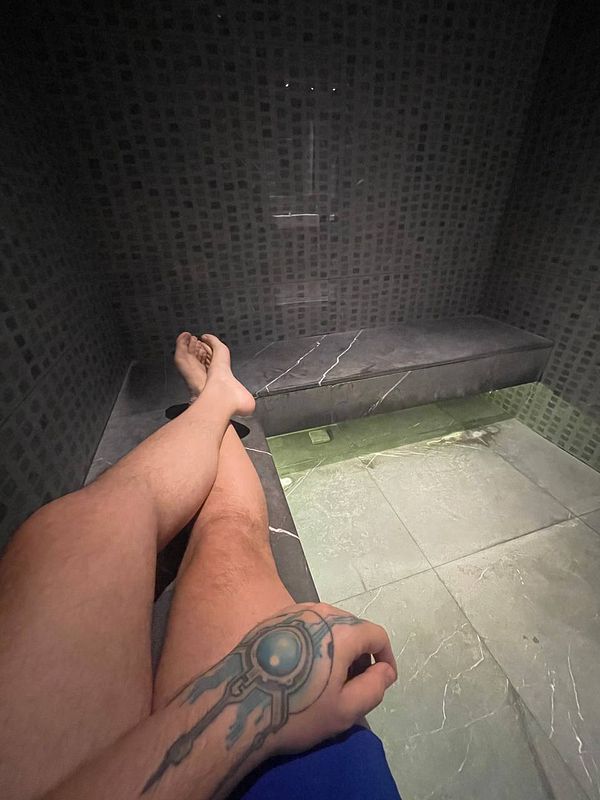A person relaxing in a steam room with a tattoo visible on their arm.