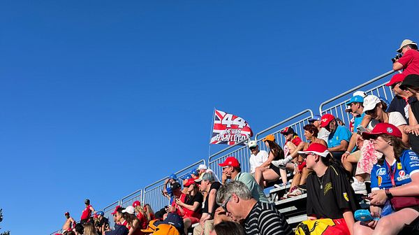 A crowd of Formula 1 fans is gathered in the stands, enjoying a sunny day at the Monza racetrack.
