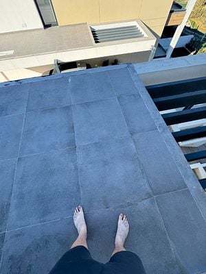 A person stands barefoot on a rooftop terrace overlooking a modern building.