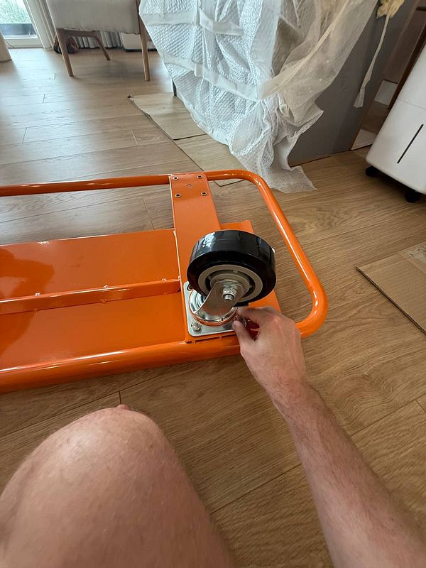 A person is assembling a wheel on an orange carriage frame.