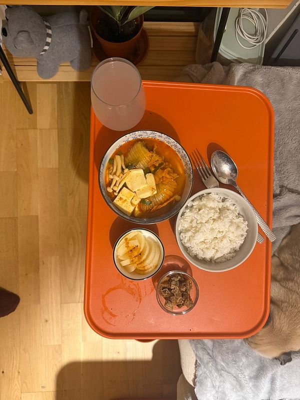 A cozy meal setup featuring kimchi-jjigae, rice, and side dishes on an orange tray.