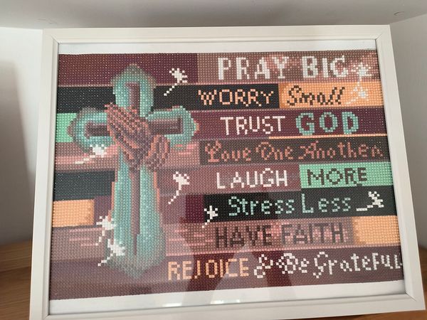 A framed decorative piece featuring a cross and inspirational phrases.