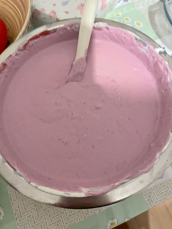 A bowl filled with pink ice cream mixture and a wooden spatula inside it.