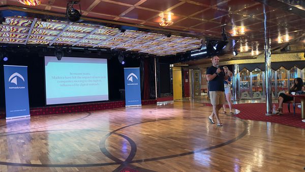 A speaker presents on stage about the impact of digital nomads on Madeira's community during a Nomad Cruise event.