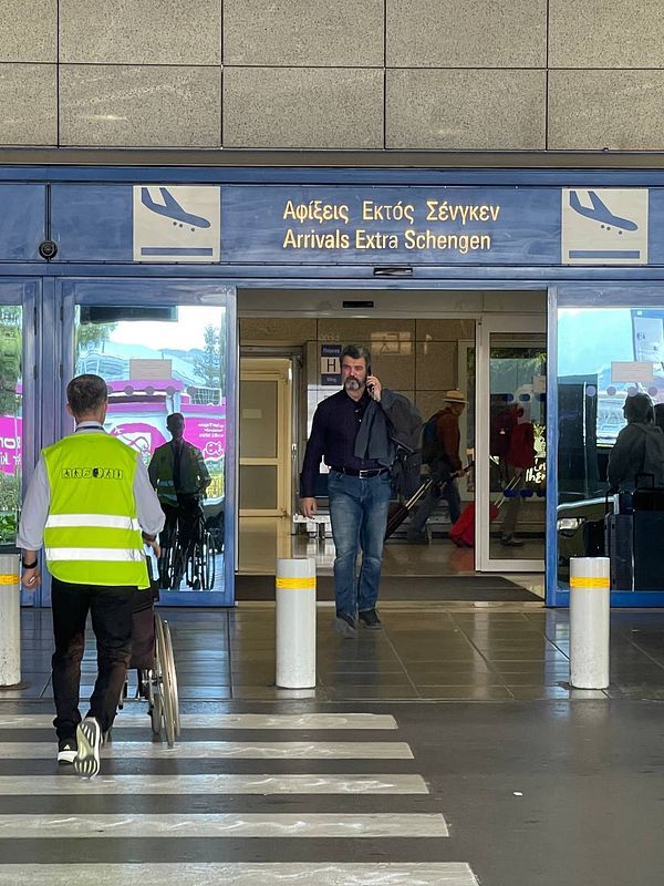 A busy airport arrival area in Greece with travelers and staff.