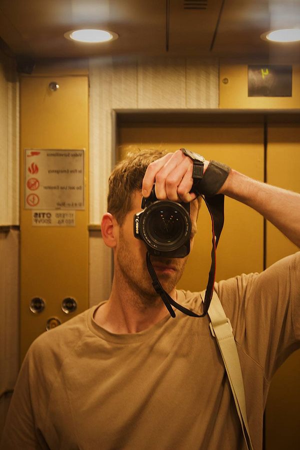 A person is taking a selfie in an elevator while holding a camera.