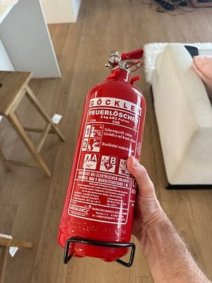 A person is holding a red fire extinguisher labeled for various fire types.