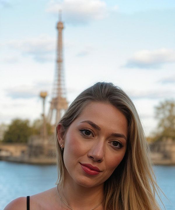 A young woman poses in front of the Eiffel Tower with a serene expression.