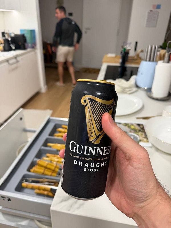 A hand holds a can of Guinness beer in a kitchen setting.
