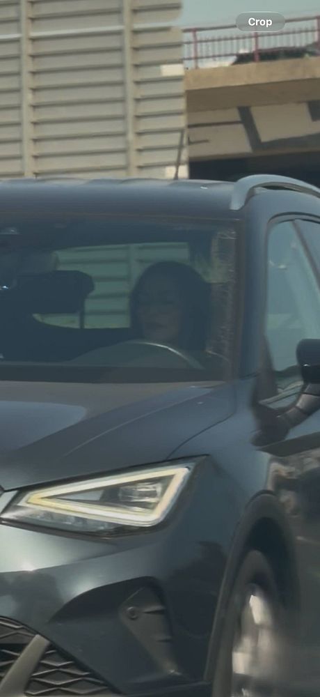 A woman is driving a dark-colored car on a highway while looking down at her phone.
