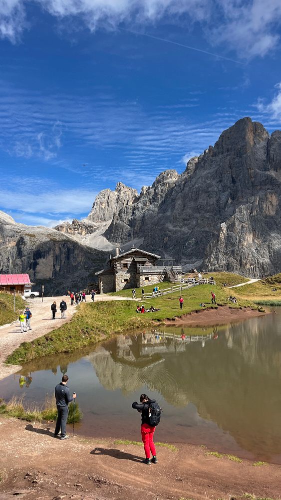 A scenic mountain landscape featuring hikers, a rustic cabin, and a reflective pond.
